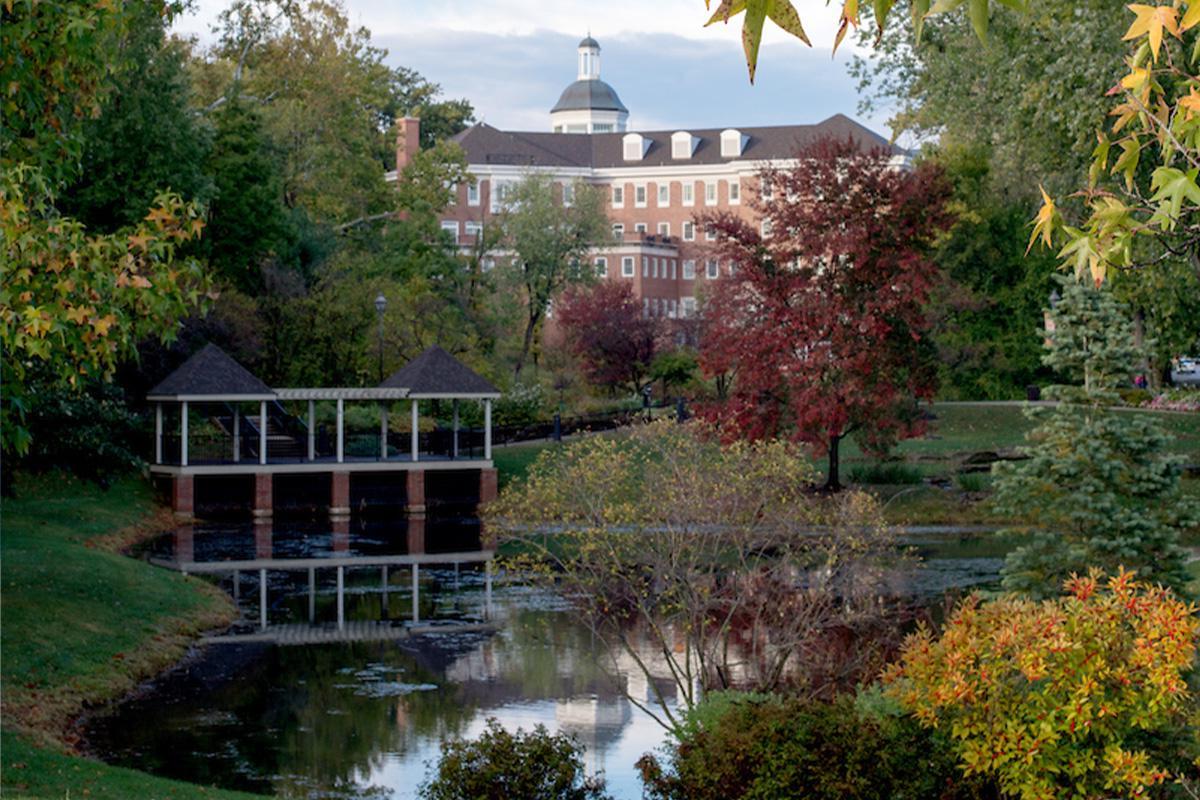 bet8九州登录入口埃默里蒂公园, featuring fall foliage surrounding a small pond on campus, with a brick building in the background